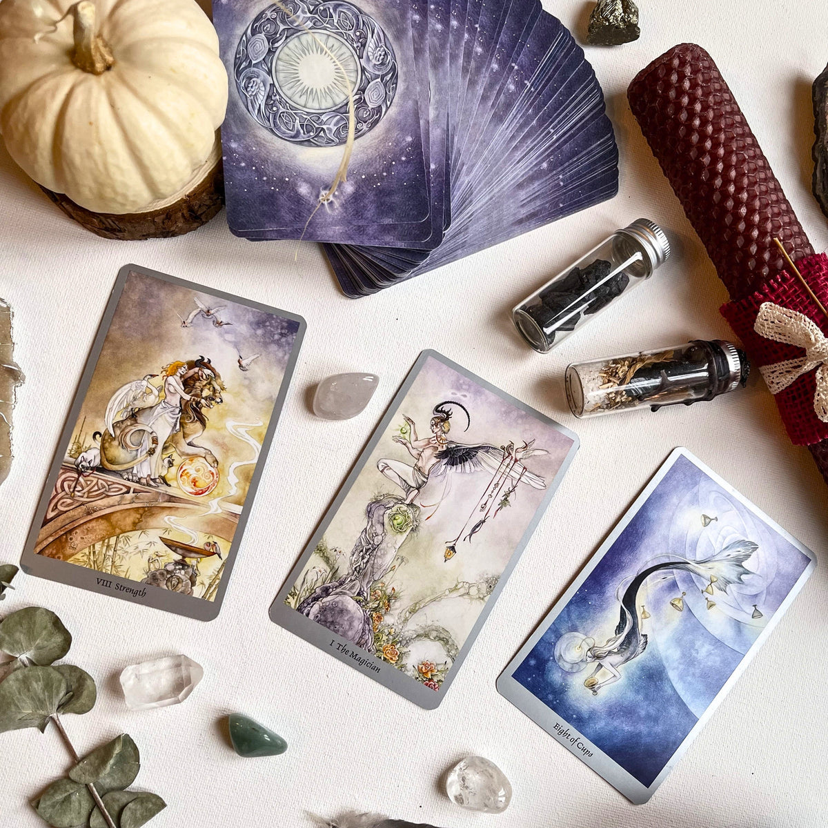 Tarot card spread featuring fairies, lions, and mermaids. Surrounding the tarot is a white background with crystals, bottles, and a wax candle. Photo by veronika-malchevska