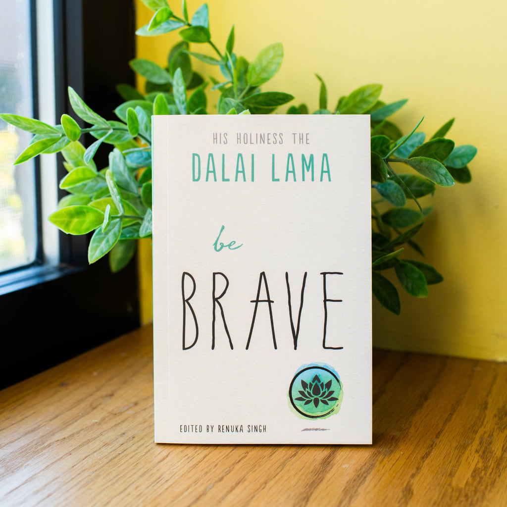Book titled 'be BRAVE' by Dalai Lama on a wooden surface with a plant in the background