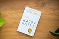 Book titled 'be HAPPY' by Dalai Lama on a wooden surface with leaves.
