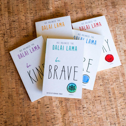 Multiple copies of 'be BRAVE' book by Dalai Lama on a cork surface