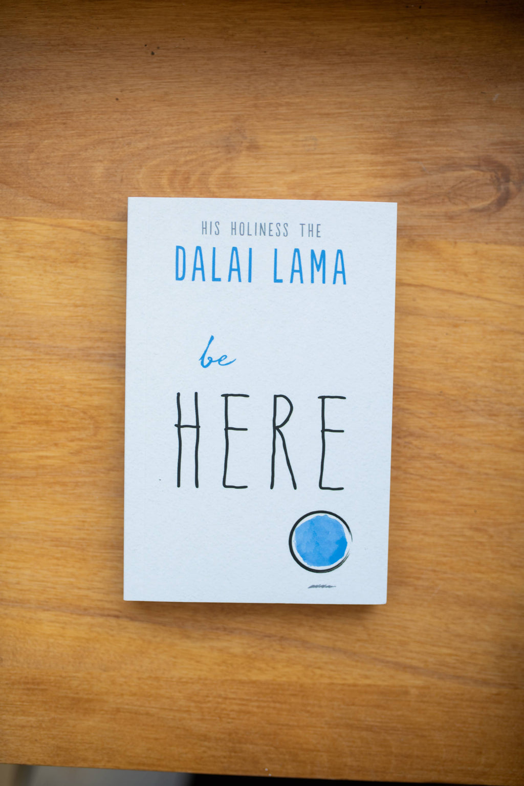 Book titled 'be HERE' by Dalai Lama on a wooden surface
