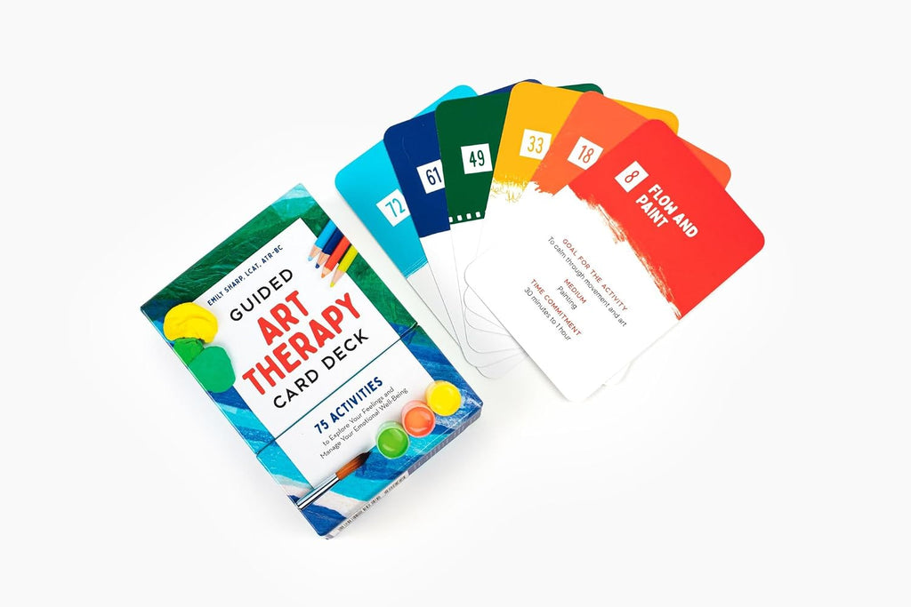 A boxed art therapy card deck with several colorful cards fanned out beside it on a clean white background. The box reads 'Guided Art Therapy Card Deck' and the cards show activity prompts with numbers and titles like 'Flow and Focus.