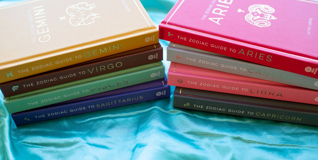 Stacks of books titled 'The Zodiac Guide' on a blue fabric background