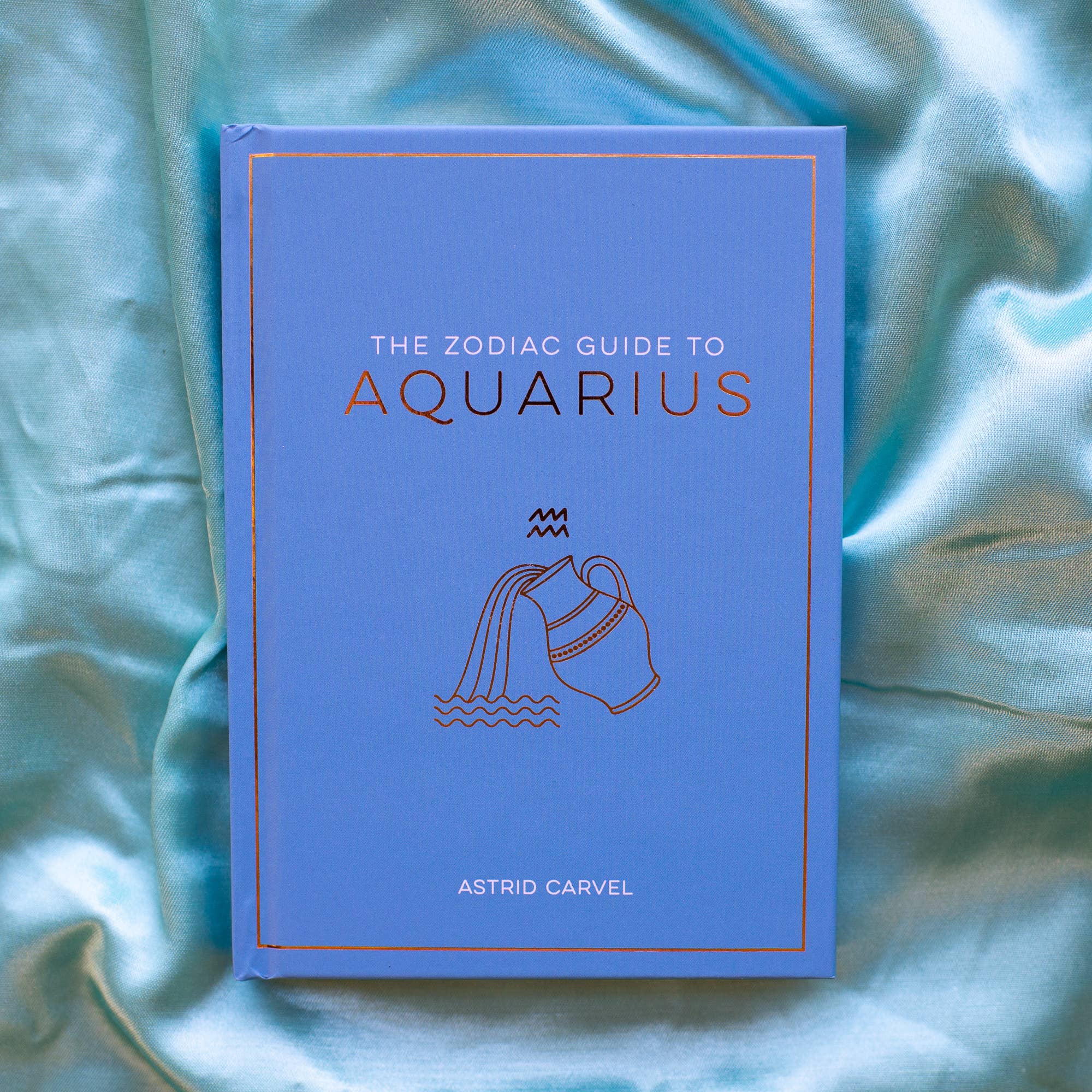 Book titled 'The Zodiac Guide to Aquarius' by Astrid Carvel on a textured blue fabric background