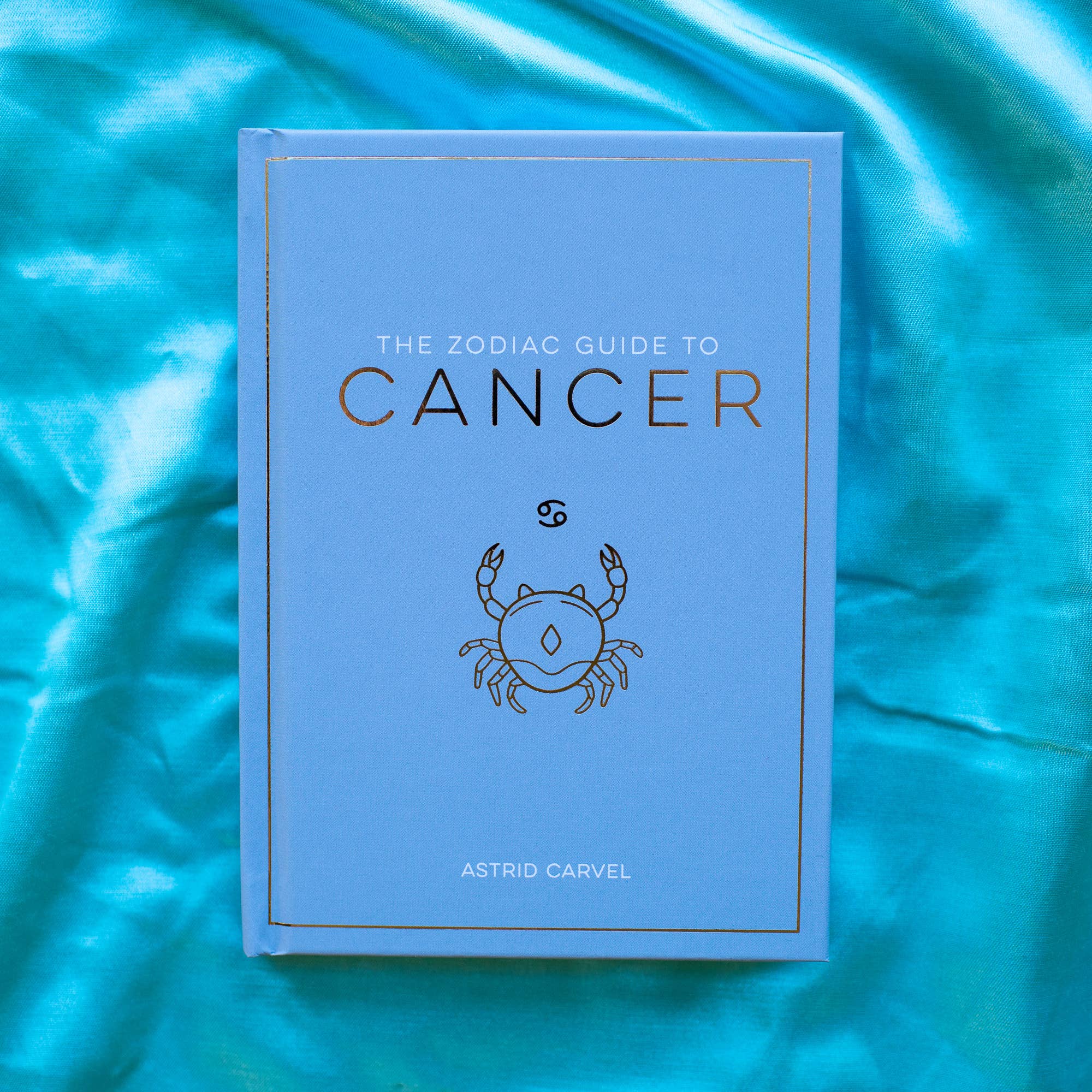 Book titled 'The Zodiac Guide to Cancer' on a blue fabric background