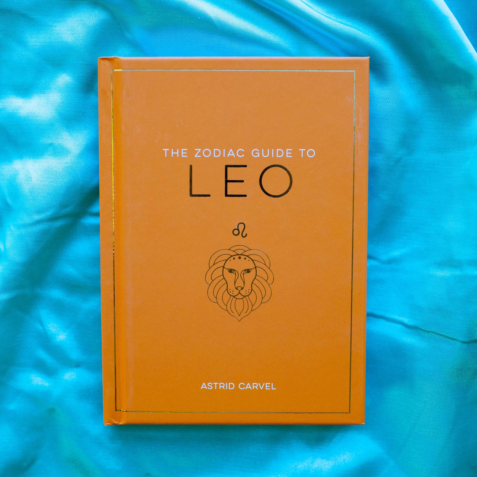 Book titled 'The Zodiac Guide to Leo' by Astrid Carvel on a blue fabric background