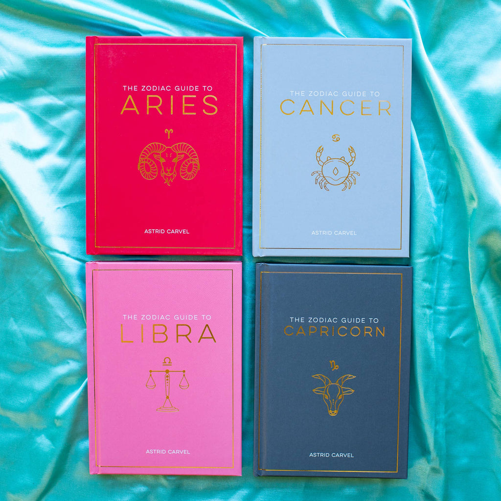 Four zodiac guide books on a turquoise fabric background