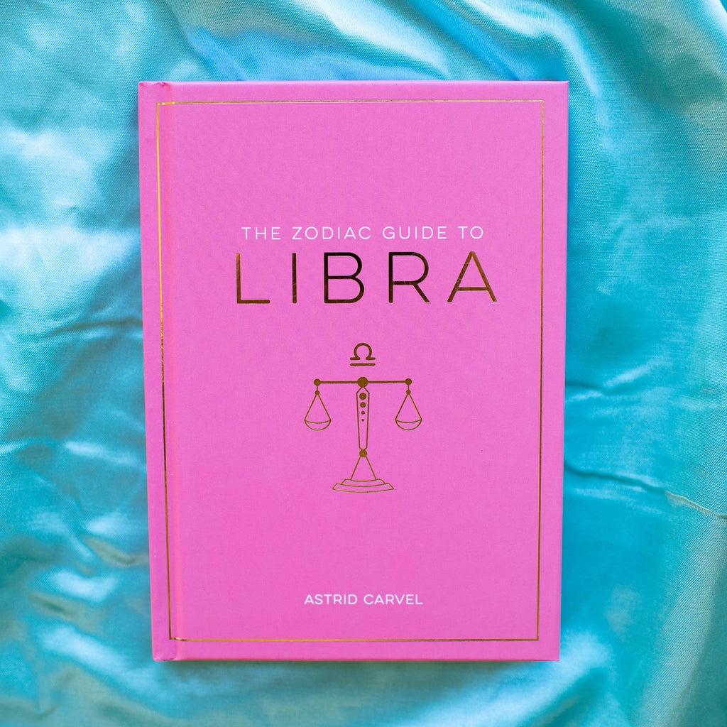 Pink book titled 'The Zodiac Guide to Libra' by Astrid Carvel on a blue fabric background