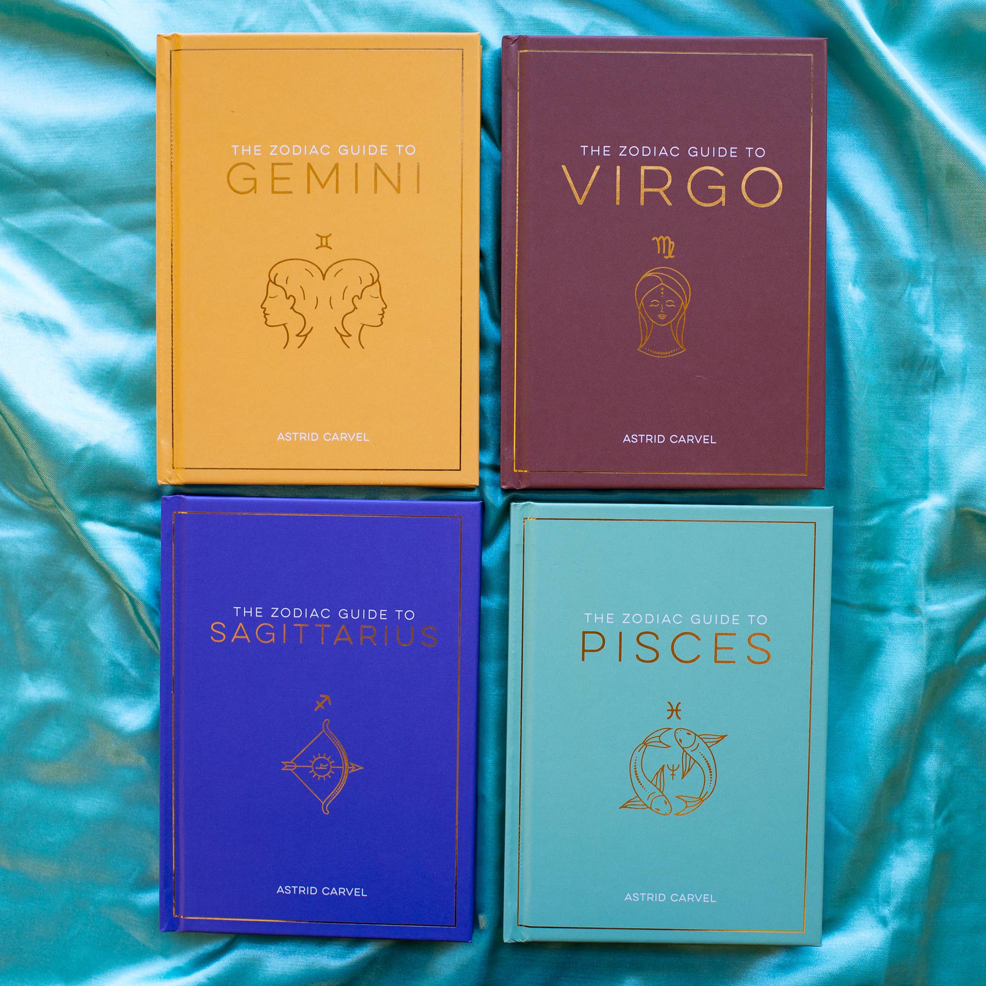 Four books on astrology by Astro Carvel on a blue satin background