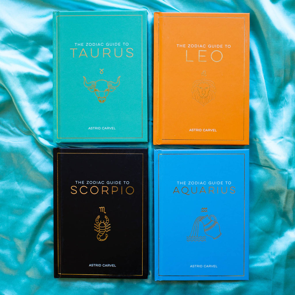 Four zodiac guide books on a textured blue surface