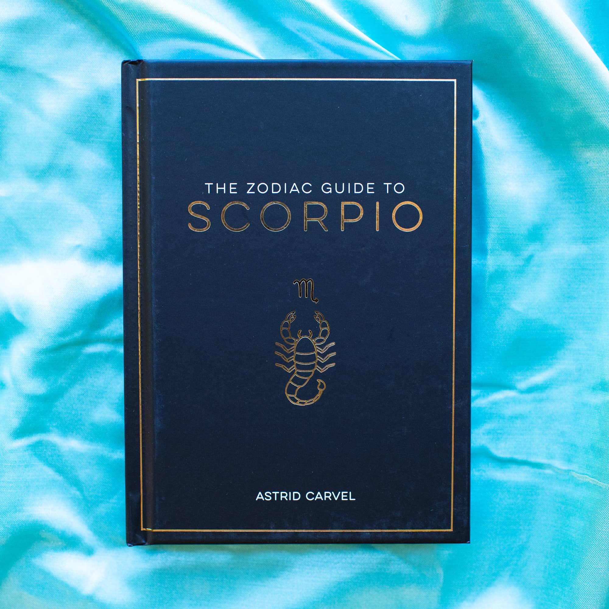 Book titled 'The Zodiac Guide to Scorpio' by Astrid Carvel on a blue textured background
