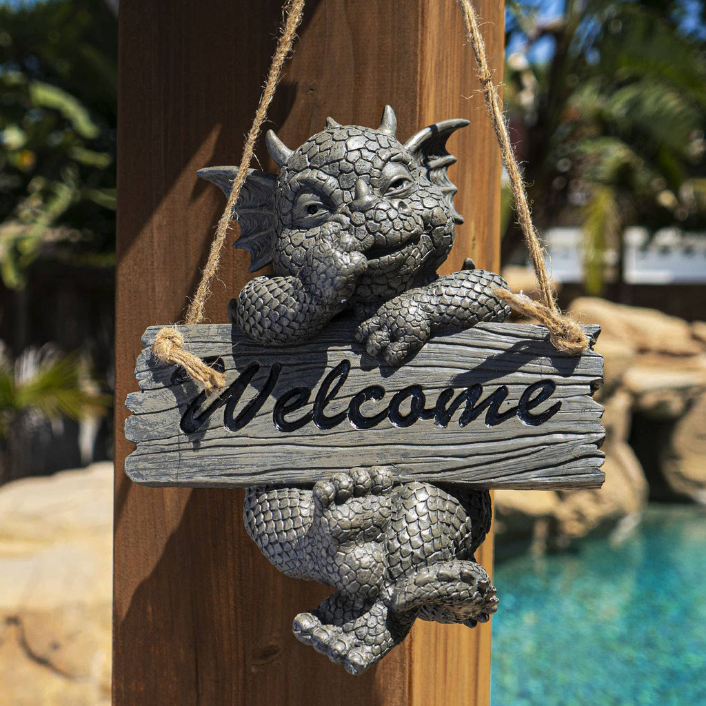 Gargoyle figurine with 'Welcome' sign hanging on a wooden post by a pool.